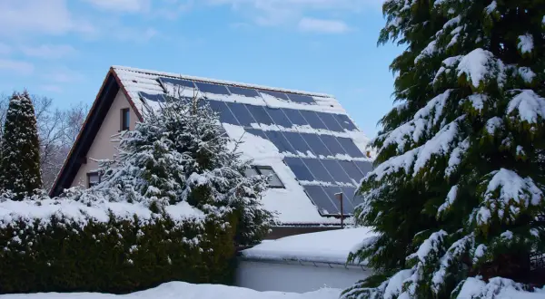 Schneebedeckte Solaranlage auf einem Hausdach, die zeigt, wie man im Winter heizen kann.