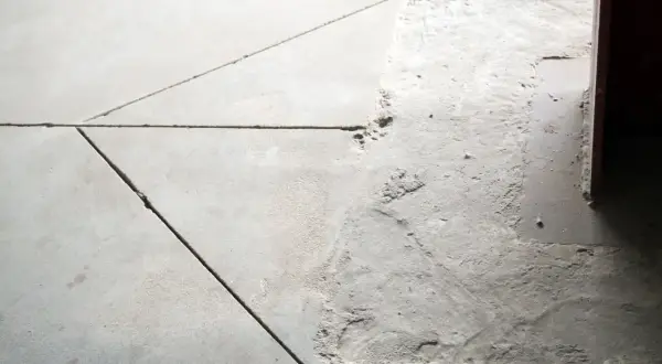 Widoczne pęknięcia i nierówności na posadzce betonowej, wskazujące na potrzebę wykonania dylatacji.