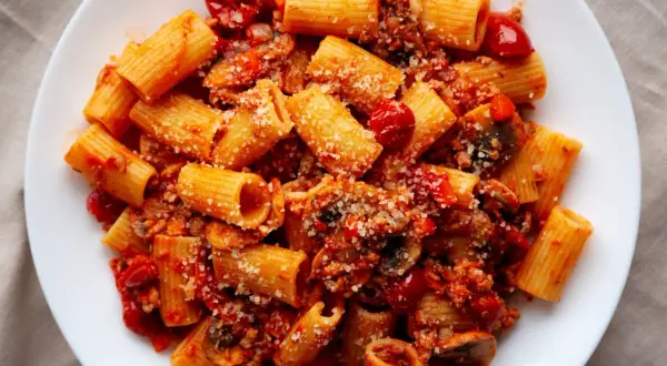 Pyszny obiad z mięsa mielonego z makaronem rigatoni w sosie pomidorowym, posypany parmezanem.