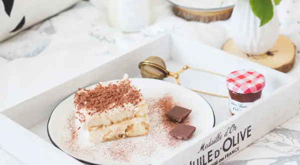 Pyszne tiramisu z biszkoptami, posypane kakao i czekoladą, na tacy z dżemem i kwiatami. Idealne na leniwe popołudnie.