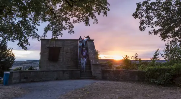 Menschen steigen die Treppen zum schlosskeller herrenberg hinauf, während die Sonne bei einem dramatischen Abendhimmel untergeht.