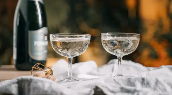 Dwa kieliszki z musującym winem, jeden z borówkami, obok butelka i korek. Czy wino musujące to szampan?