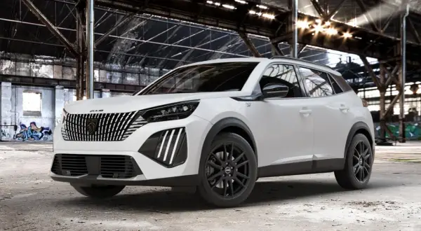 Biały Peugeot 2008 GT z czarnymi felgami stoi w opuszczonej hali przemysłowej, gdzie światło przebija się przez dach.
