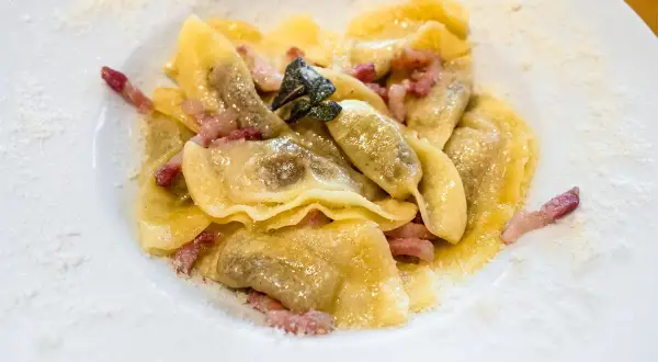 Casoncelli alla bergamasca, pasta ripiena con pancetta e salvia, spolverati di parmigiano su un piatto bianco.