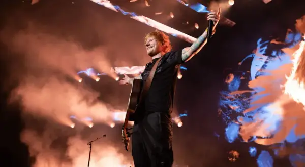Ed Sheeran na koncercie w Polsce, grając na gitarze i pozdrawiając publiczność.