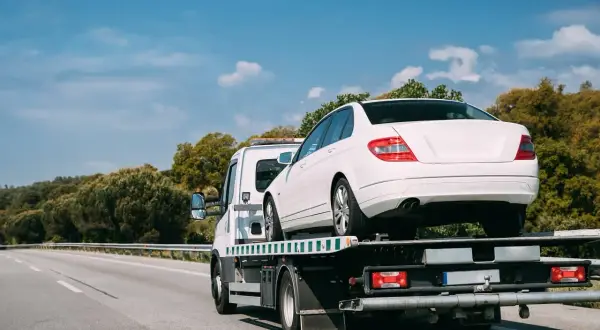 Laweta holująca biały samochód osobowy na autostradzie.