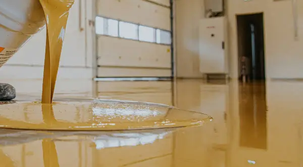 Liquido giallo, probabilmente resina epossidica cos'è, cola da un secchio su un pavimento lucido in un capannone.