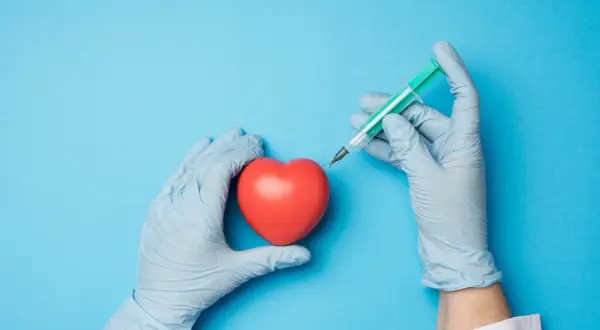 Mains gantées tenant un cœur rouge et une seringue, évoquant une intervention comme une coronarographie.