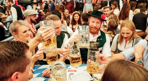 Ludzie w tradycyjnych strojach bawią się na Oktoberfest, wznosząc kufle piwa.