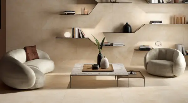 Ein modernes Wohnzimmer in warmen Beigetönen. Ein geschwungenes Sofa und ein Sessel laden zum Entspannen ein. Regale mit Büchern und Deko schmücken die Wand.
