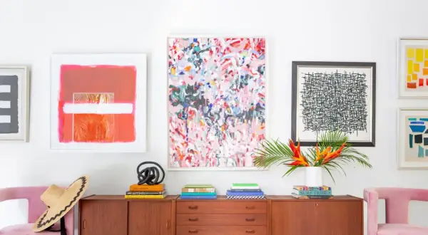 Vibrant abstract art and graphic prints adorn a wall above a midcentury credenza, showcasing a stylish blend of midcentury graphic design.