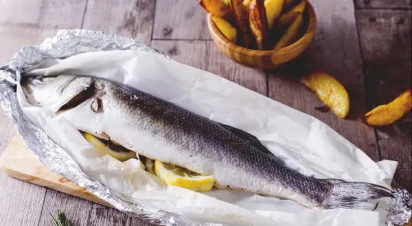 Gegrillter Seebarsch mit Zitrone, bereit für den köstlichen Geschmack. Dazu knusprige Kartoffelspalten.