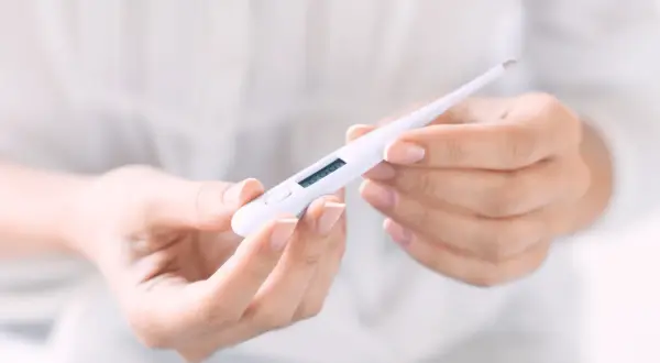 Hände halten ein digitales Thermometer, das die Temperatur für den Eisprung anzeigt.