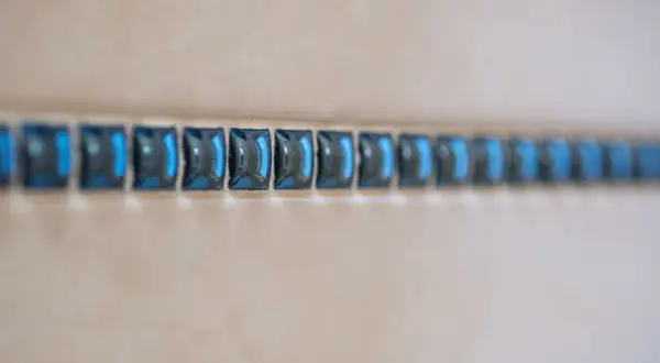 Ligne de petites mosaïques bleues, comme une frise, à une certaine hauteur sur un mur de salle de bain.