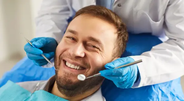 Uśmiechnięty mężczyzna u dentysty. Badanie stomatologiczne, które może pomóc rozwiać wątpliwości dotyczące implantów zębowych a nowotworów.