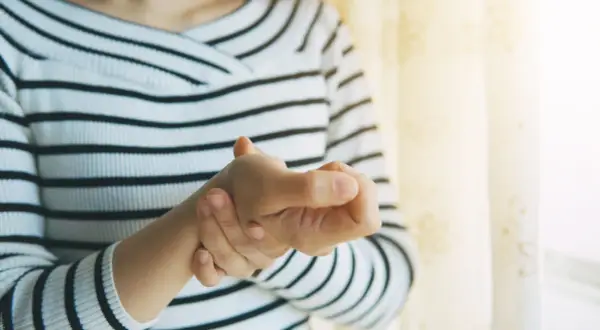 Frau hält ihren Daumen, der schmerzt, als ob sie einen Schnappfinger Daumen hätte.
