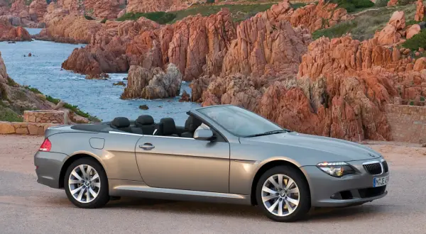 Szary kabriolet BMW E63 na tle skalistego wybrzeża z turkusową wodą.