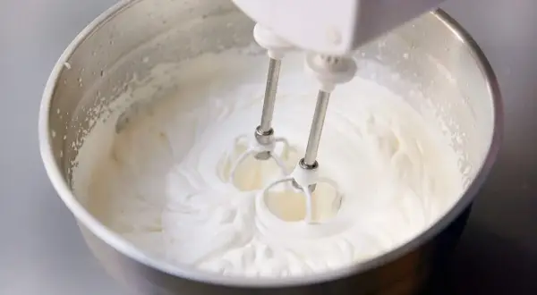 Schlagobers wird mit einem Handmixer in einer Edelstahlschüssel aufgeschlagen. Die cremige Masse ist bereit für süße Köstlichkeiten.