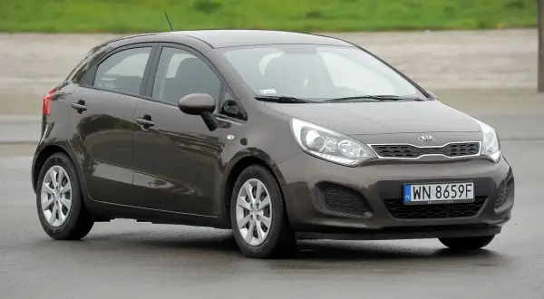 Brązowe kia rio 3 na mokrej nawierzchni, z widocznym numerem rejestracyjnym WN 8659F.