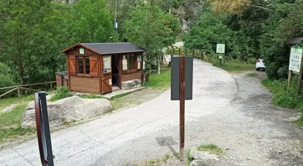 Caseta de información y señalización para senderismo en Aigüestortes. Un camino de grava y asfalto se adentra en un bosque frondoso.