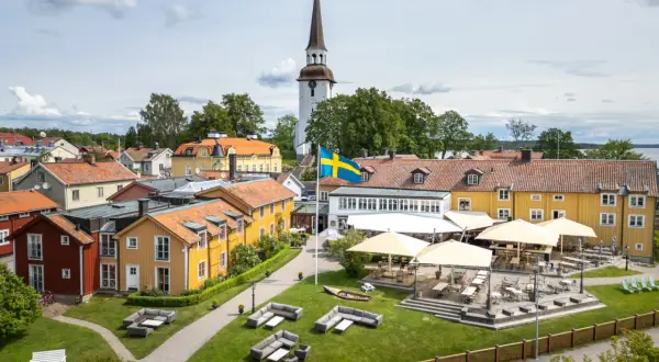 Mariefreds Värdshus med svensk flagga och kyrktorn. Uteservering med parasoller och sittgrupper i gräset.