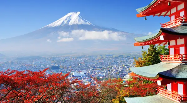 Malownicze widoki Japonii: góra Fudżi w chmurach, miasto i czerwone liście klonu obok czerwonej pagody.