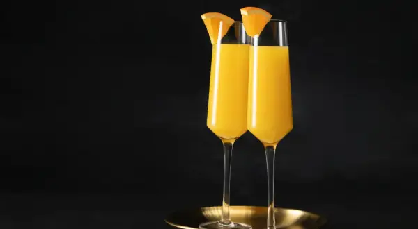 Dwa kieliszki wypełnione złocistym płynem, ozdobione plasterkami pomarańczy. Idealny duet na brunch, klasyczny mimosa.