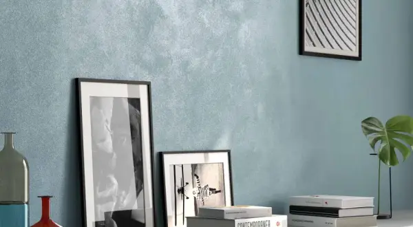 Parete con pittura effetto sabbiato azzurra, arricchita da quadri, vasi e libri. Ottime opinioni per questo stile.