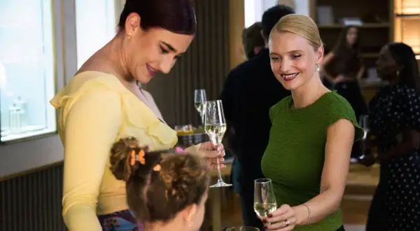 Två kvinnor och ett barn minglar med glas. Kvinnan i gult ler mot barnet, medan kvinnan i grönt håller upp sitt glas. Kanske en scen ur danska serier.