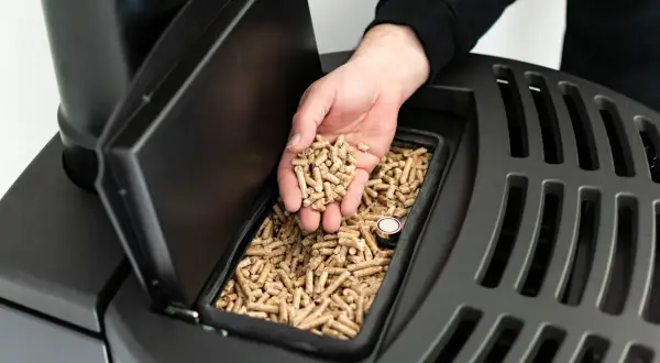 Dłoń wsypuje pellet do pieca. Czyste powietrze dzięki dofinansowaniu do pieca na pellet.