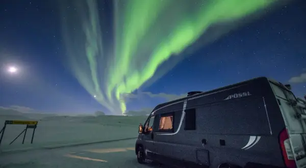 Ein Wohnmobil steht unter dem faszinierenden Himmel, wo grüne **polarlichter** tanzen. Mond und Sterne leuchten über der verschneiten Landschaft.