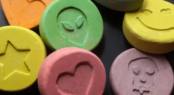 Kolorowe tabletki z symbolami: serce, gwiazda, kosmita, uśmiech, czaszka. To mogą być tabletki MDMA.