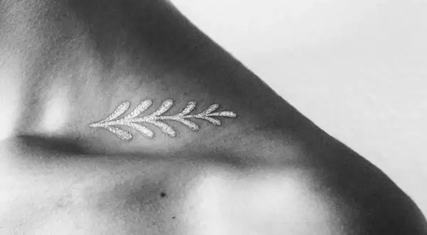 Delicado diseño de rama con **tatuajes blancos en piel negra**, resaltando la delicadeza y el contraste en el hombro.