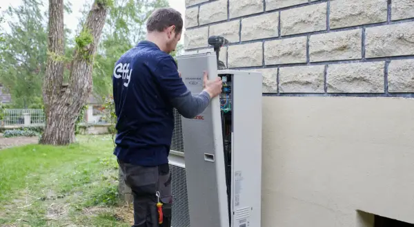 Un technicien installe une pompe à chaleur. La distance avec la maison du voisin est prise en compte pour le bruit.