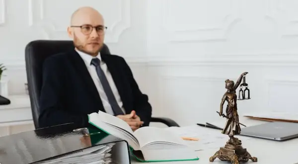 Prawnik w garniturze siedzi przy biurku, obok stosu dokumentów i otwartej księgi. Zastanawiasz się, ile kosztuje notariusz?