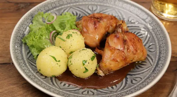 Saftiger Hasenbraten Hausfrauenart mit Klößen, Salat und dunkler Soße auf einem gemusterten Teller.