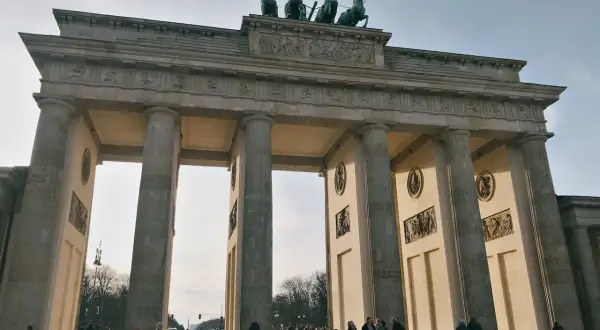 Das Brandenburger Tor, ein Meisterwerk der Klassizismus Architektur, mit seiner Quadriga auf dem Dach. Menschen spazieren davor.
