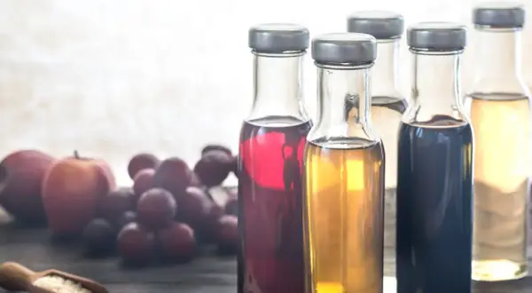 Flaschen mit verschiedenen Essigsorten, Äpfel und Trauben. Essigwasser gesund für den Körper.
