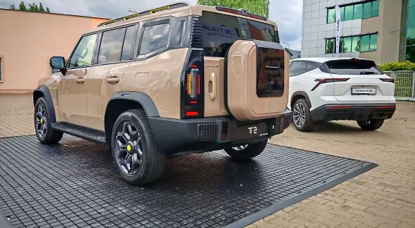 Beżowy Jetour T2 z kołem zapasowym z tyłu, obok białego SUV-a. Sprawdź Jetour T2 cena i dostępne opcje.