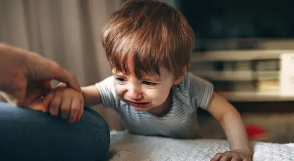 Małe dziecko płacze, gdy mama wychodzi. Trzyma się jej ręki, nie chcąc jej puścić.