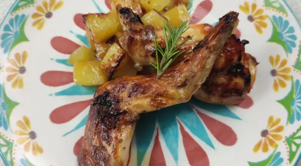 Roasted rabbit pieces with golden potatoes and a rosemary sprig on a colorful floral plate.