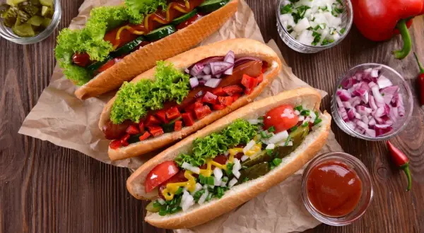 Trzy apetyczne hot dogi z sałatą, pomidorami, ogórkiem, cebulą i papryką. Idealne na letnie grillowanie!