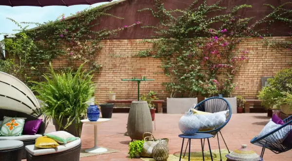 Acogedor **diseño terraza exterior** con muebles de ratán, sillas azules, plantas exuberantes y detalles decorativos en ladrillo.