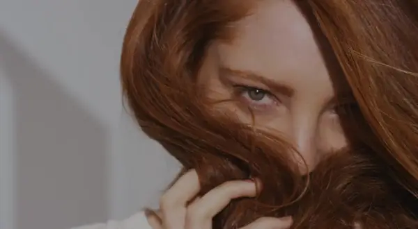 Occhi penetranti emergono da una cascata di capelli ramati, un invito a scoprire come fare il rosso scuro perfetto.