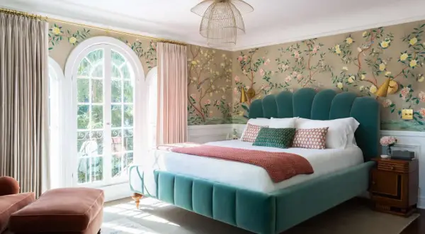 Chinoiserie wallpaper with birds and blossoms offers stunning bedroom wall decor ideas. A teal velvet bed and pink curtains complete the elegant look.