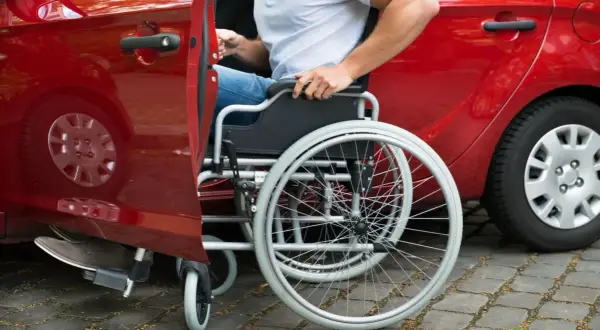 Persona in sedia a rotelle si avvicina a un'auto rossa, modello 104, per salire.