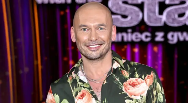 Tomasz z "Tańca z Gwiazdami" w kwiecistej koszuli, uśmiechnięty na tle sceny.