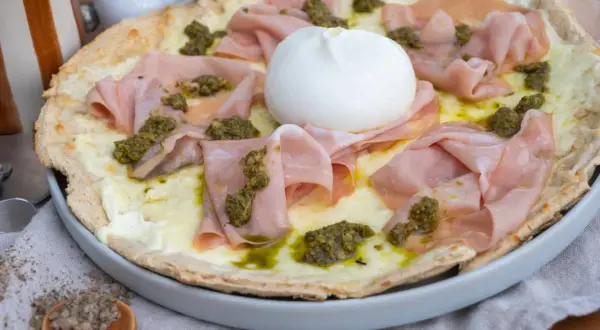 Pizza mit Burrata, Mortadella und Pesto auf einem Teller.