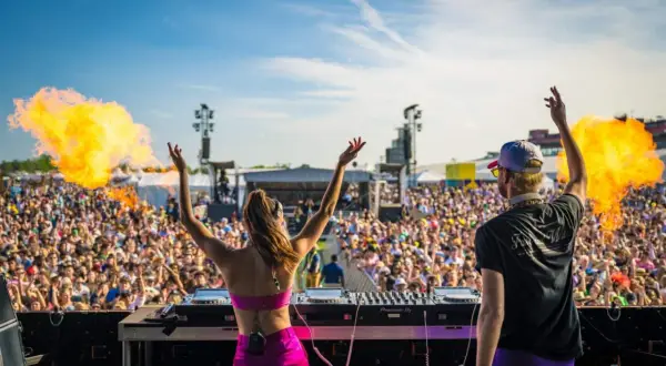 DJ-ka i DJ na scenie, tłum szaleje na festiwalu techno. Wybuchy ognia dodają energii.
