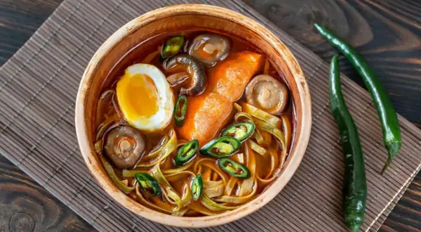 Eine Schüssel Ramen mit Ei, Pilzen und Chili. Der würzige Sud weckt die umami zunge und verspricht ein intensives Geschmackserlebnis.